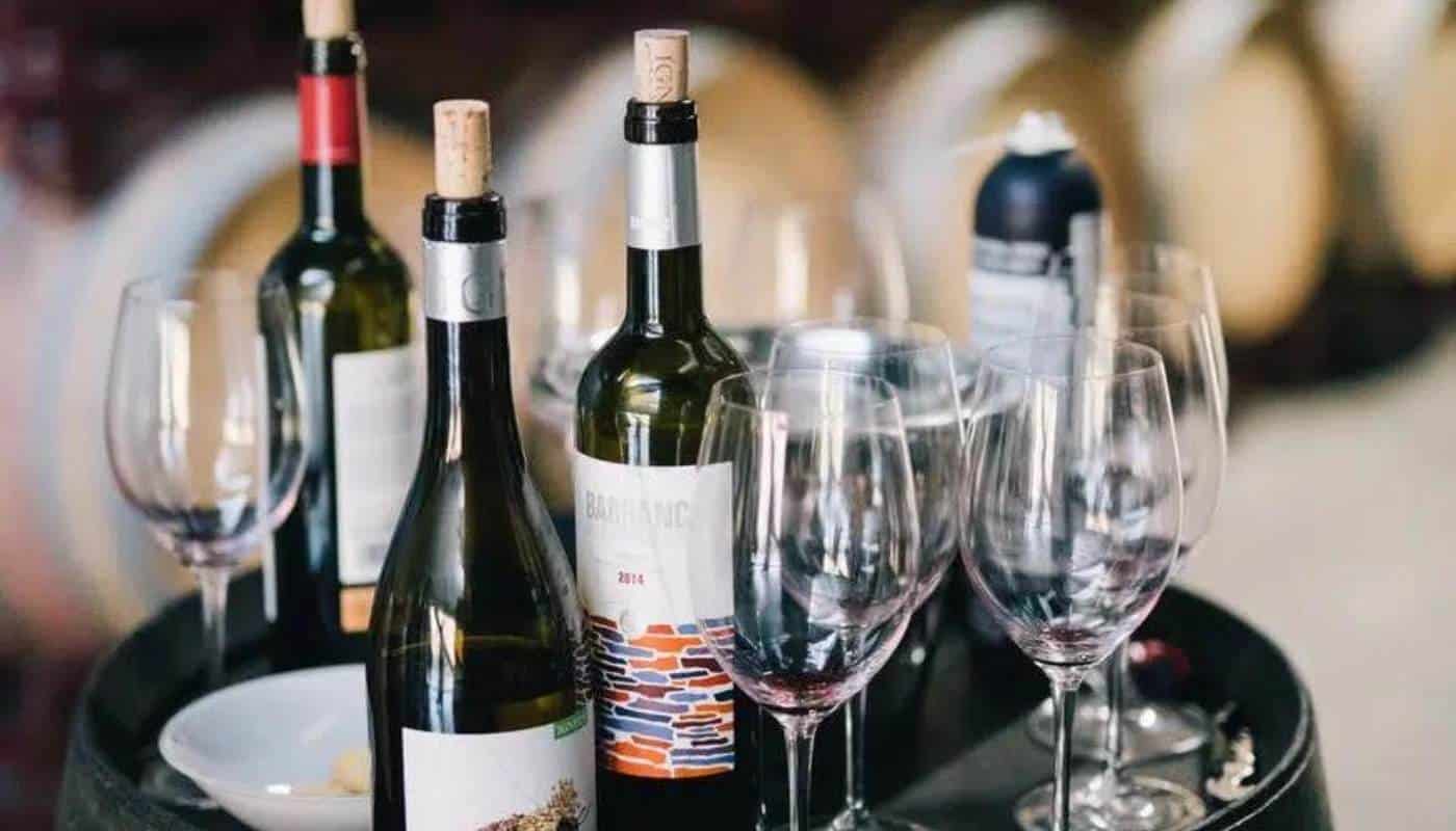 Wine bottles and empty wine glasses arranged on a barrel in a cellar