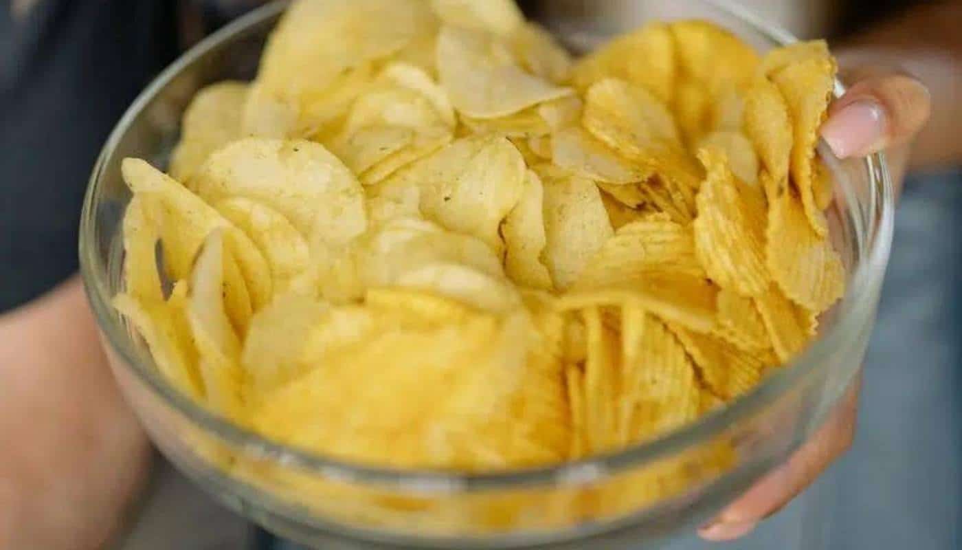 Hands holding a glass bowl heaped with potato chips