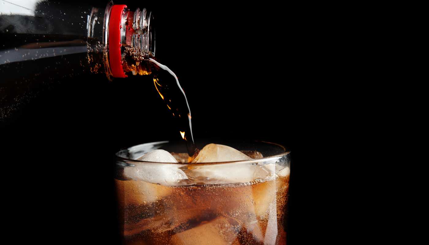 Cola being poured from a bottle into a glass filled with ice
