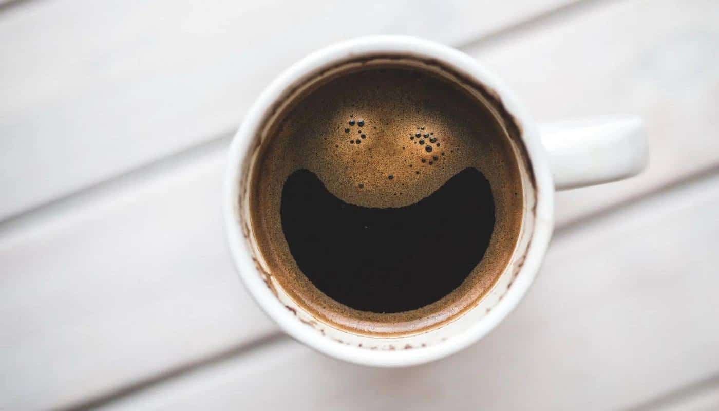 A mug of black coffee seen from above, the crema forming a smiley face