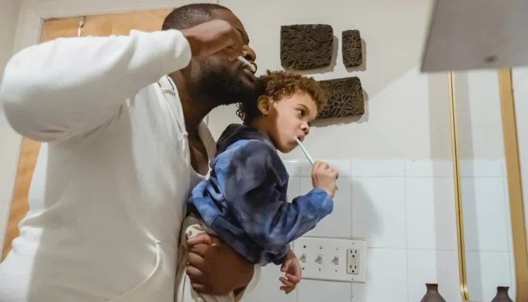 A parent holding a toddler up at the bathroom mirror while the child brushes their teeth