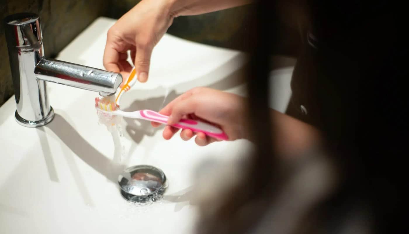 A hand rinsing a child’s toothbrush under a running tap