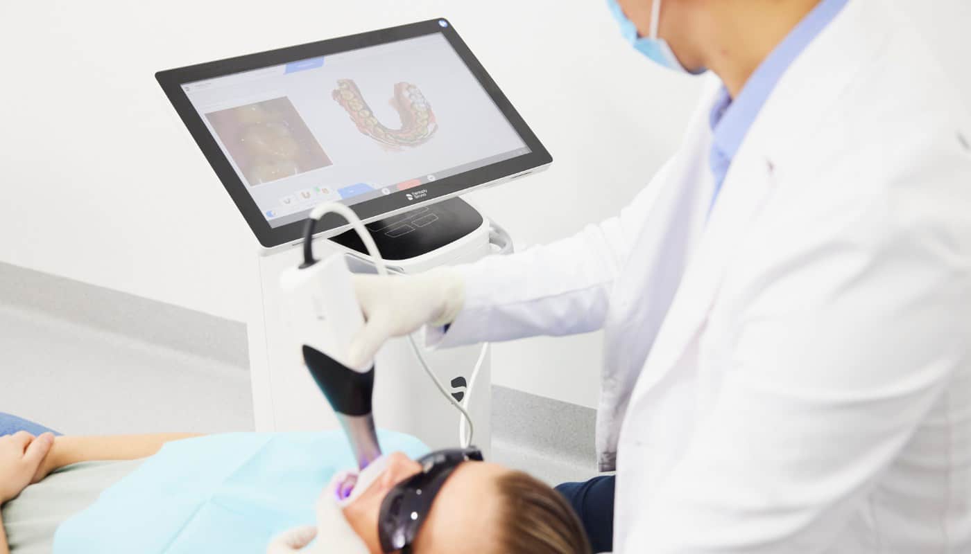 A dentist using an intraoral scanner on a patient, with the 3D scan of the dental arch shown on the screen
