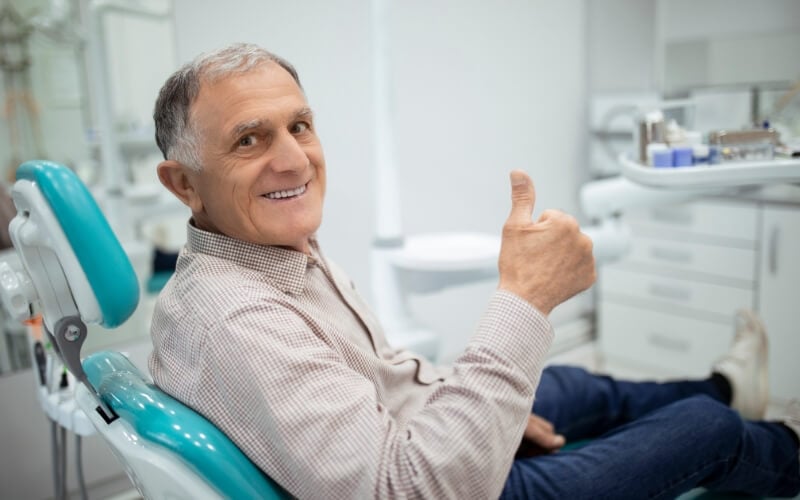 An older man giving a thumbs up while seated in the dental chair