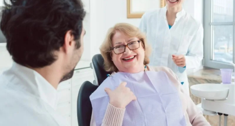 An older woman giving a thumbs up from the dental chair beside her dentist and assistant