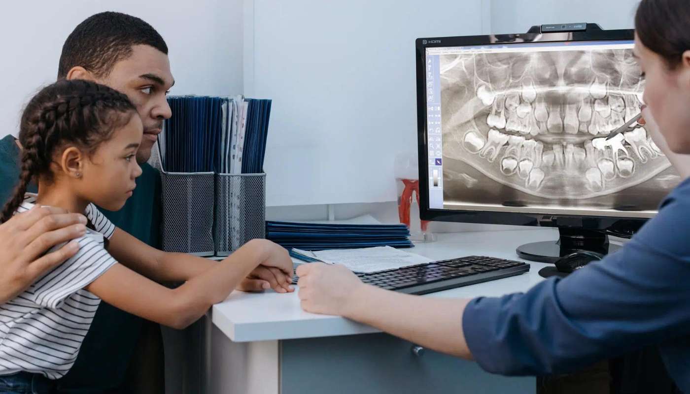 A dentist showing a panoramic x-ray on a screen to a parent and child