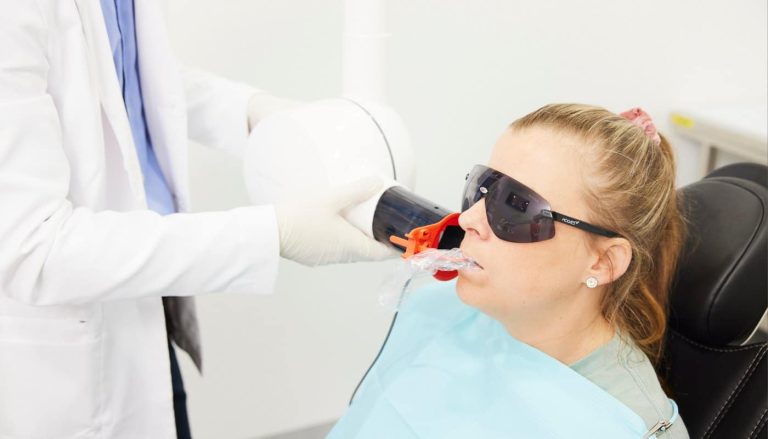 A dentist positioning an x-ray sensor for a patient wearing protective eyewear in the dental chair