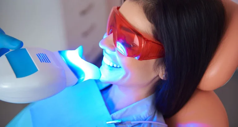 A patient in protective red eyewear undergoing light-activated teeth whitening in the dental chair