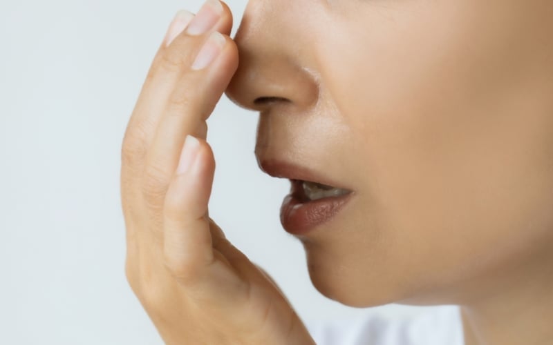 Close-up profile of a person breathing into their cupped hand to check their breath