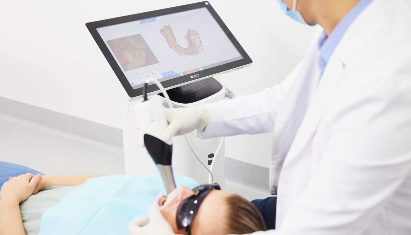 A dentist scanning a patient with a 3D intraoral scanner, the digital impression showing on the screen alongside
