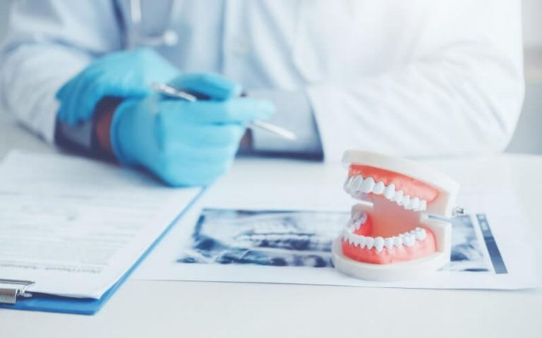 A dentist at a desk with a model of the teeth, paperwork and an x-ray