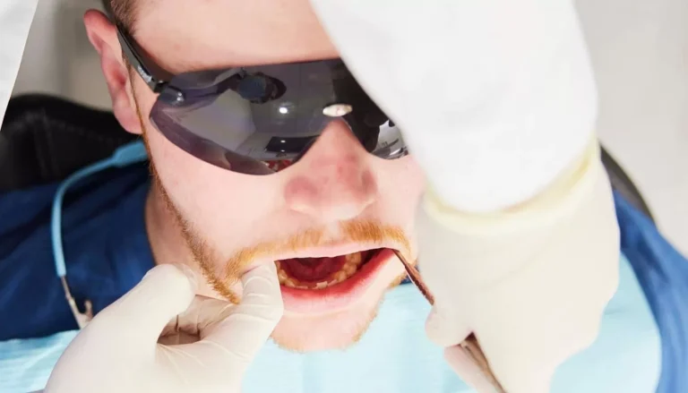 Close-up of a patient in protective glasses having their lower teeth examined with a dental probe