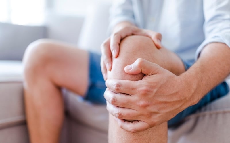 A person sitting on a sofa holding their painful knee with both hands
