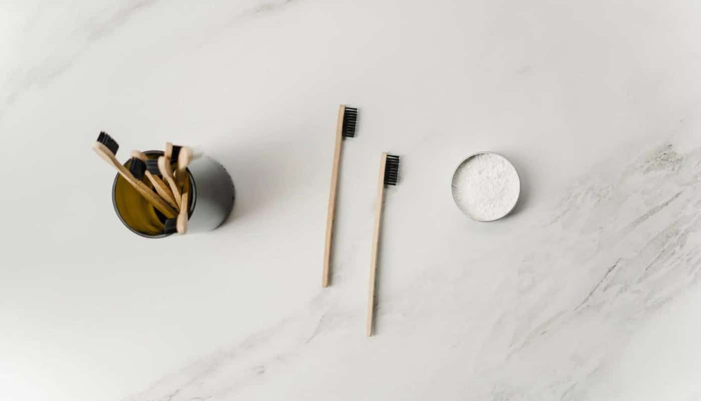 Two bamboo toothbrushes laid out on a marble surface beside a holder and a tin