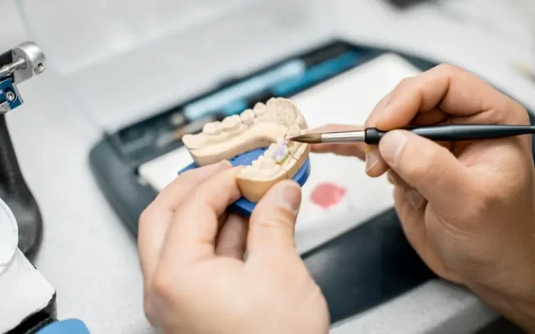 A dental technician shaping a prosthesis mounted on an articulator in the laboratory
