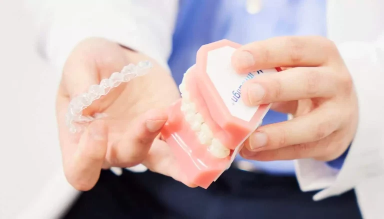 A dentist holding a clear aligner tray in one hand and a model of the teeth in the other