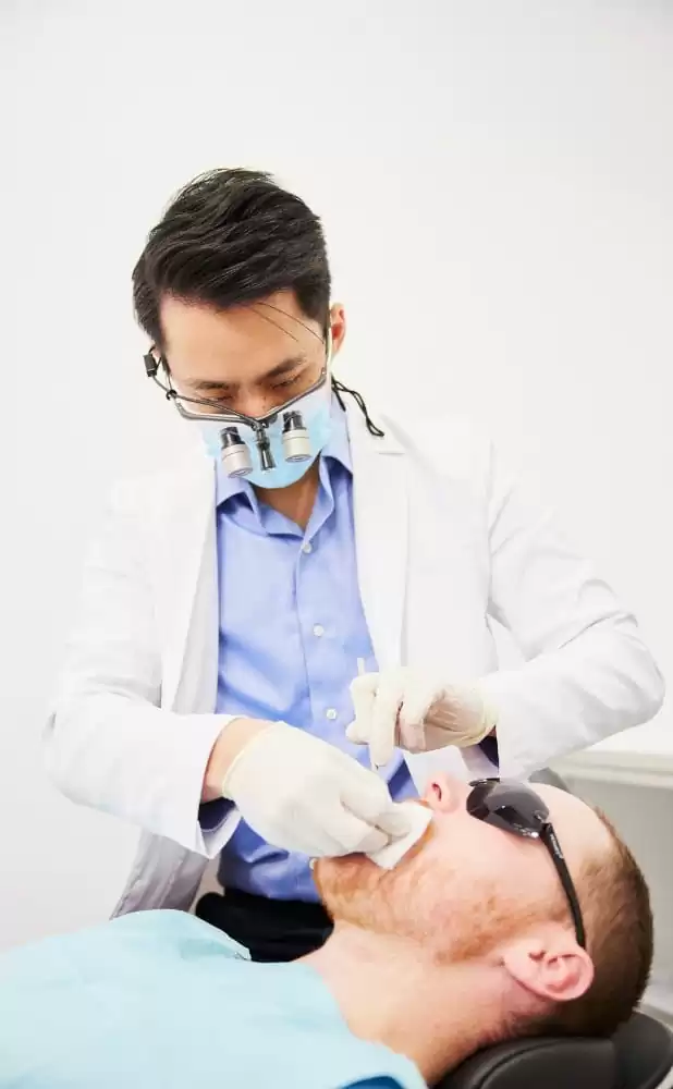 A dentist wearing magnifying loupes treating a patient reclined in the chair