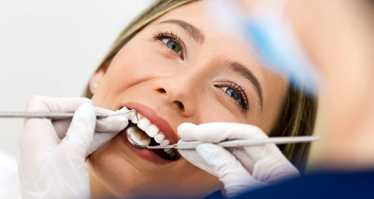 A patient smiling in the dental chair while a dentist works on her upper front teeth