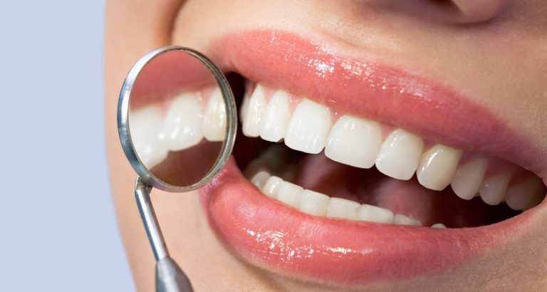 Close-up of a smile beside a dental mirror, showing even upper front teeth