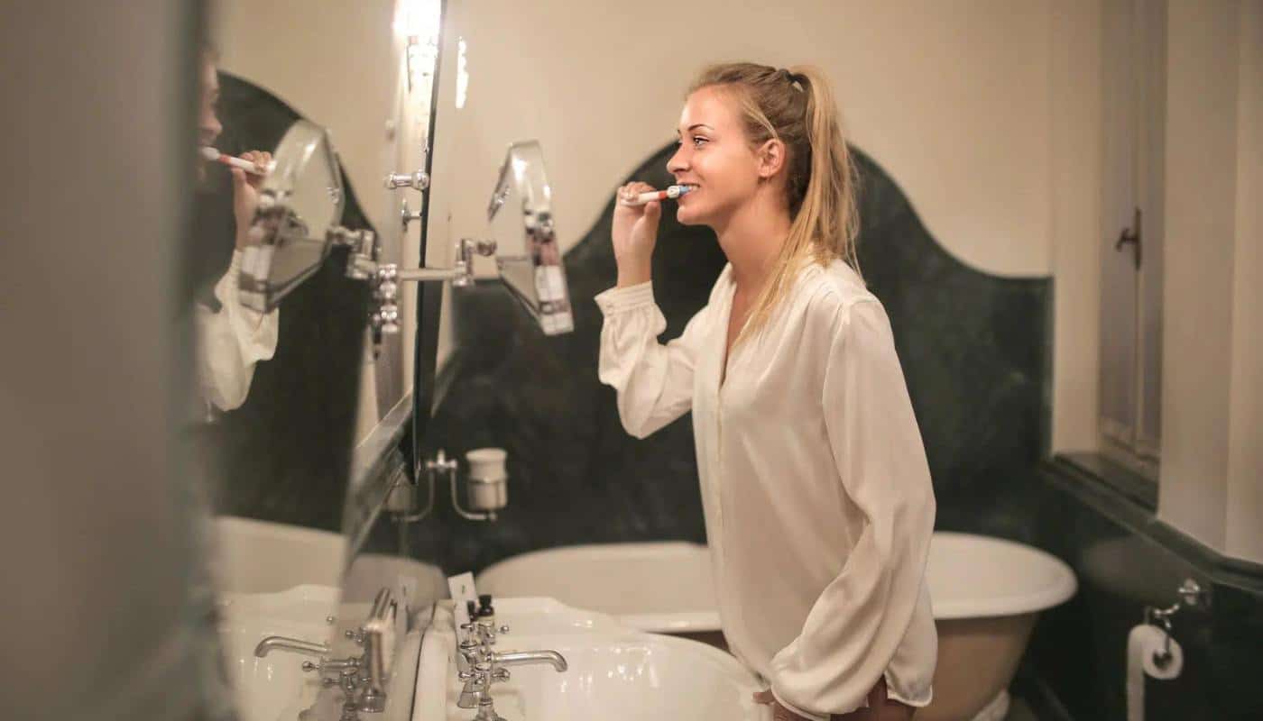 A woman brushing her teeth at a bathroom basin