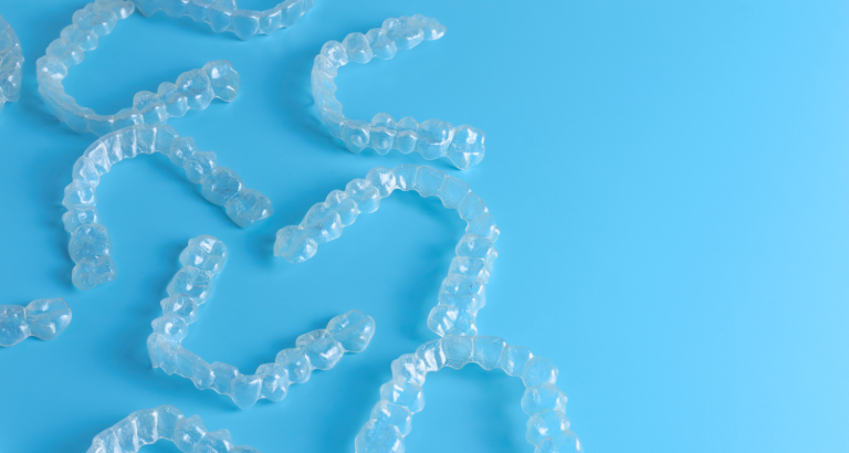 Several clear orthodontic aligner trays arranged on a blue background