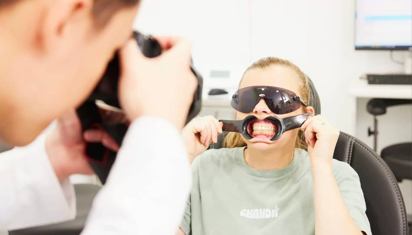 A clinician photographing a patient’s teeth while the patient holds a cheek retractor