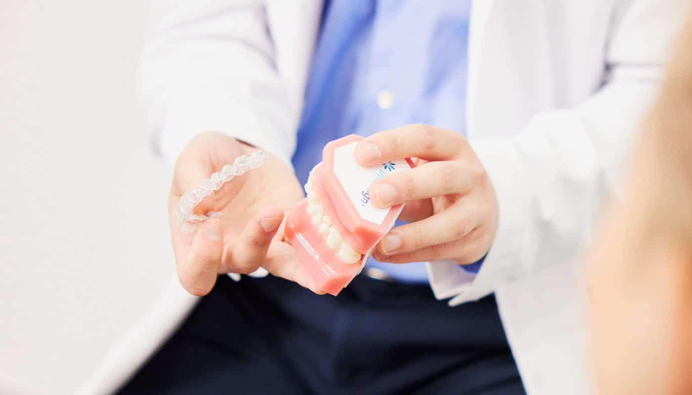 A dentist holding a clear Invisalign aligner alongside a model of the teeth