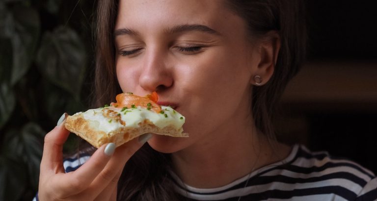 A woman biting into a slice of pizza