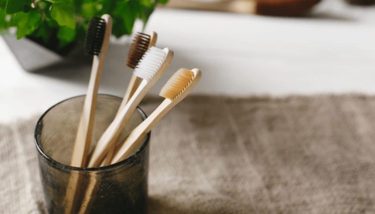 Bamboo toothbrushes standing in a glass on a bathroom bench