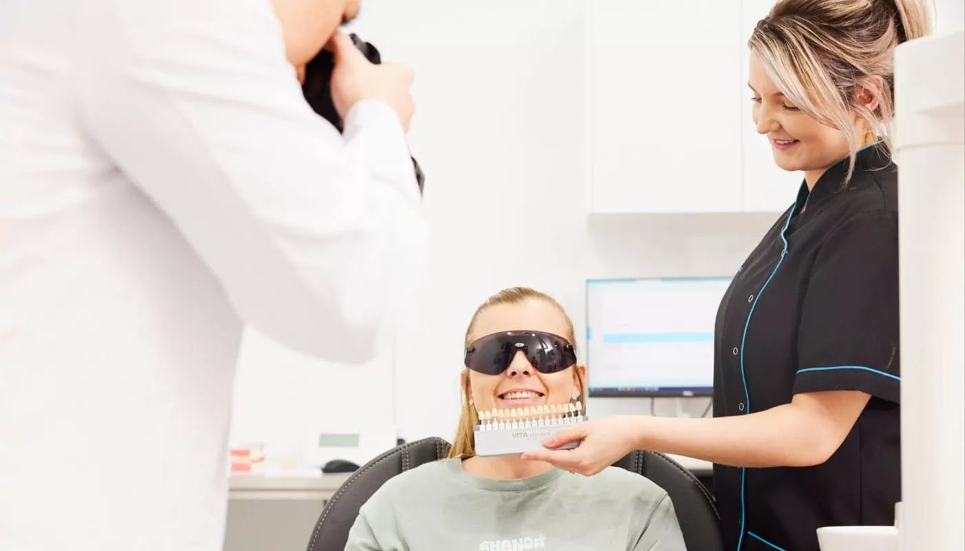 A patient in the dental chair having her tooth shade matched against a shade guide held by a dental assistant