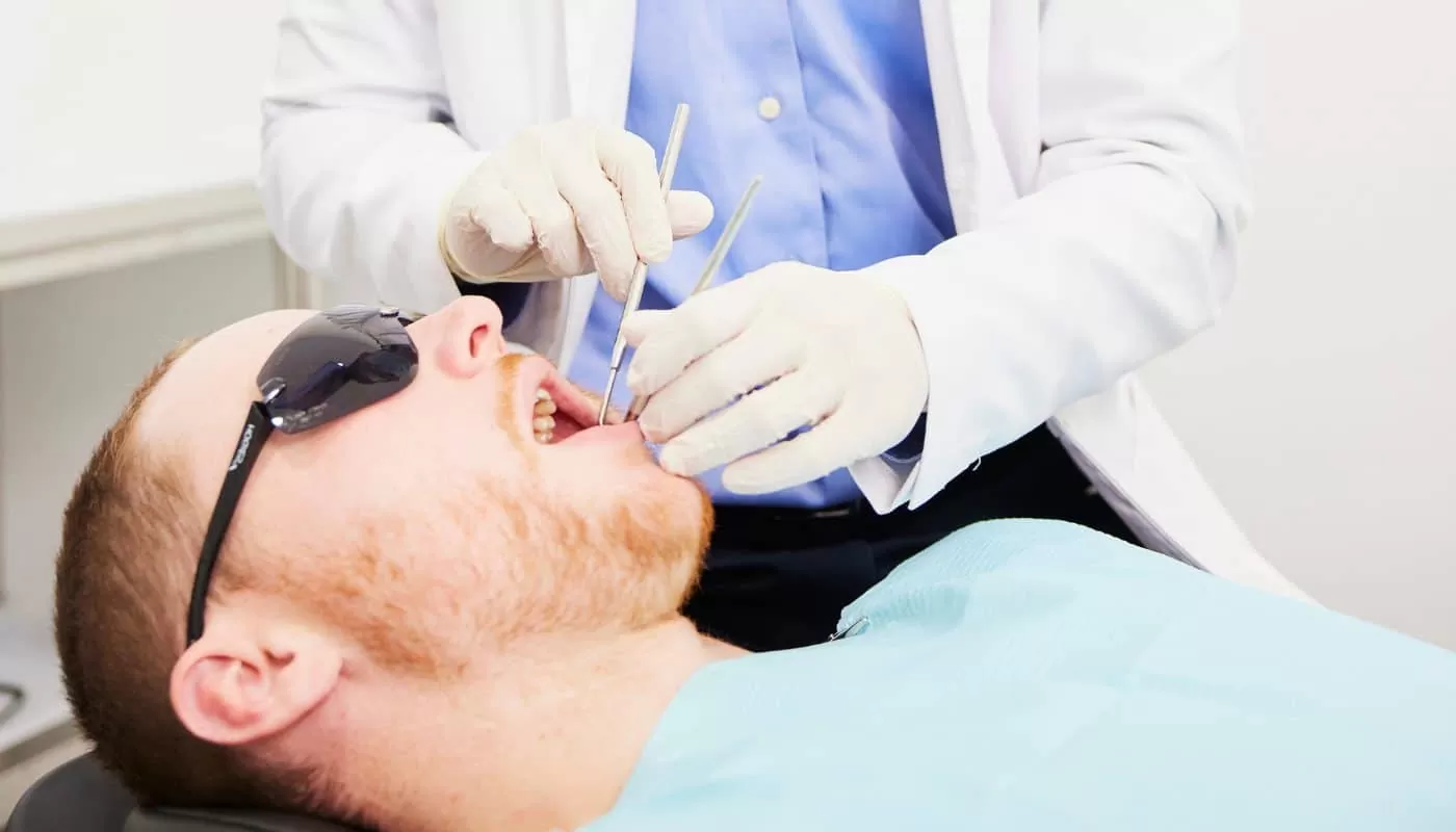 A dentist examining a reclined patient’s back teeth with a mirror and probe