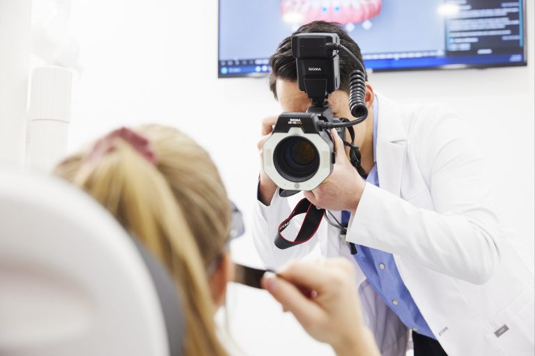 A dentist photographing a patient’s smile with a ring-flash camera for treatment planning