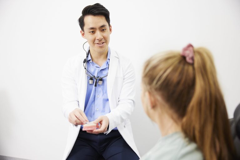 A dentist wearing loupes discussing treatment with a patient in the surgery