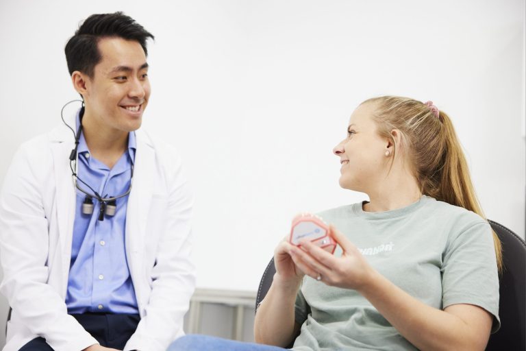 A dentist in conversation with a patient holding a clear aligner tray during a consultation