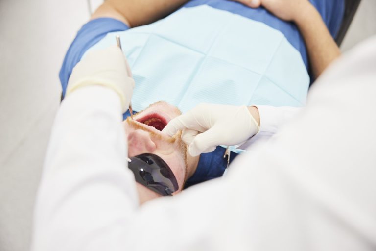 Overhead view of a dentist examining a patient’s teeth with a probe while the patient reclines in the chair