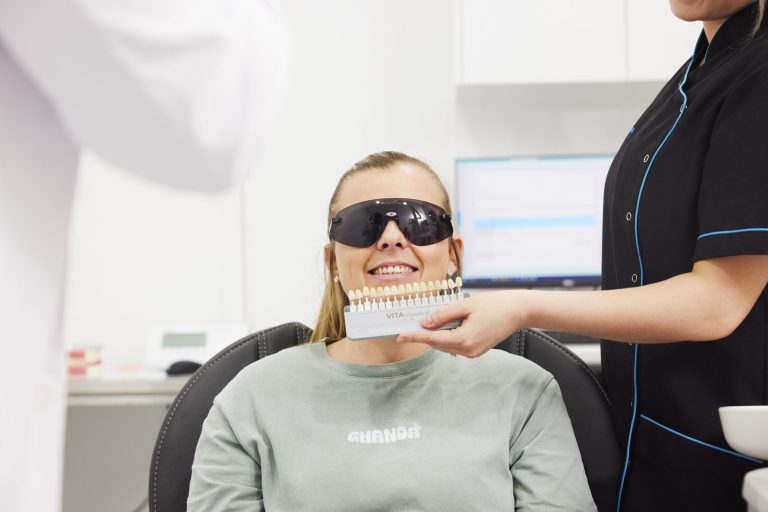 A smiling patient in the dental chair while an assistant holds a VITA shade guide beside her teeth