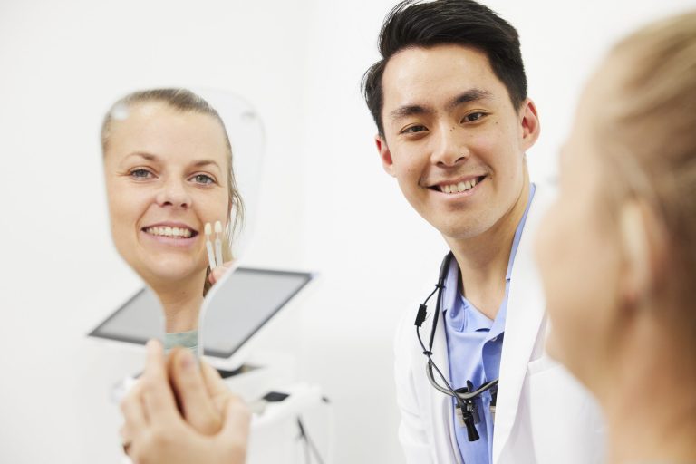 A patient looking at her smile in a hand mirror while her dentist looks on