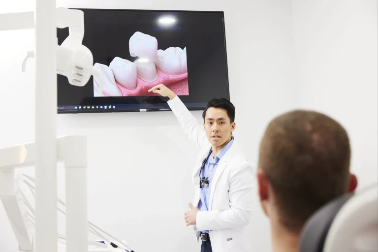 A dentist pointing to a wall screen showing a 3D animation of a crown being seated on a prepared tooth