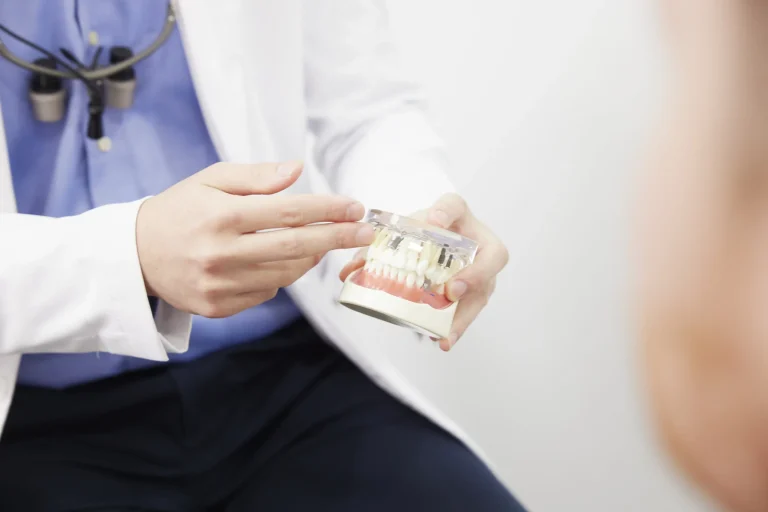 A dentist pointing to a cutaway jaw model showing implants supporting a fixed restoration