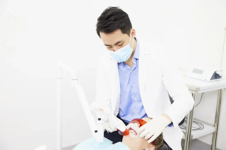 A dentist applying in-chair whitening gel while the patient wears a cheek retractor