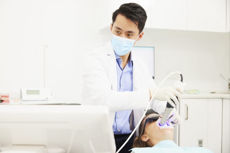 A dentist using a curing light on a patient’s teeth during in-chair whitening